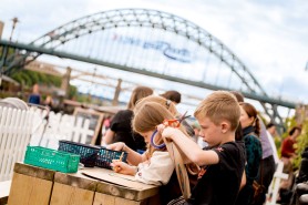 A group of children doing arts and crafts on a wooden table on Newcastle's Quayside