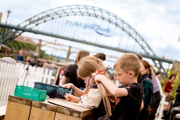 A group of children doing arts and crafts on a wooden table on Newcastle's Quayside