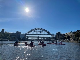 A group of people kayaking on the River Tyne with the Tyne Bridge in the background