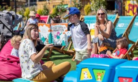 A woman reading a storybook to two children sitting on brightly coloured deckchairs