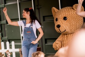A women in blue denim dungarees standing next to a person in a teddy bear costume