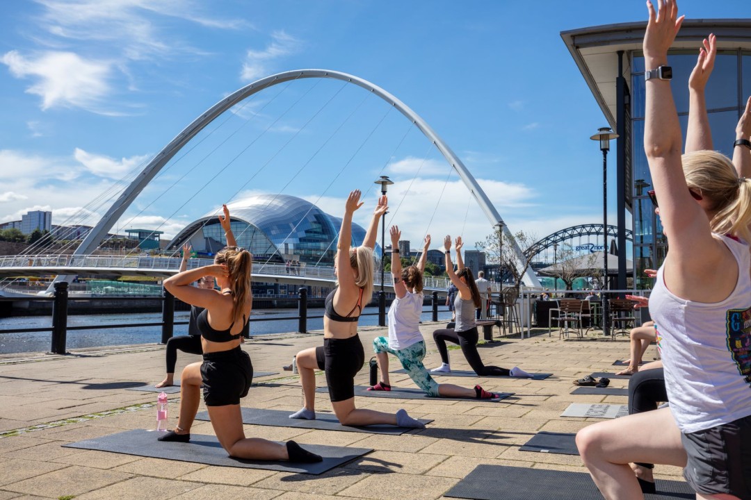 A group of women doing yoga on Newcastle’s Quayside with the Millennium Bridge in the background