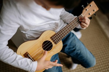 A child dressed in blue jeans and a white top playing a ukulele