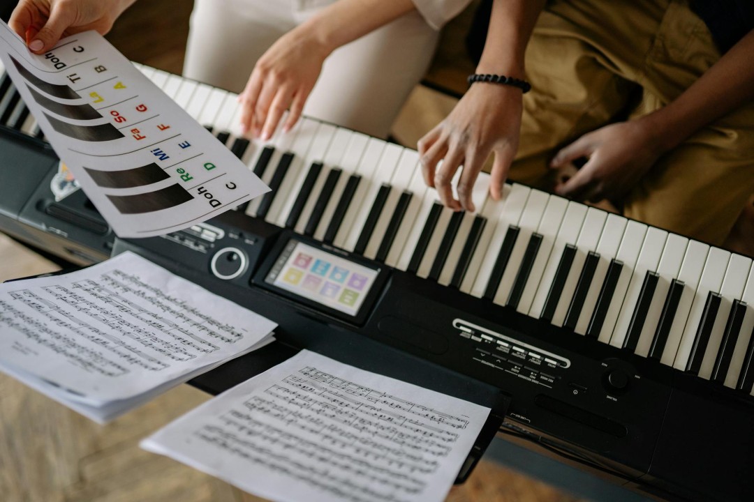 An image of a person playing a keyboard with sheet music in the foreground