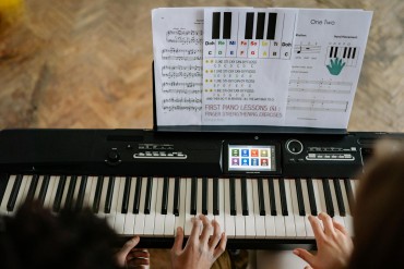 Two people playing on a keyboard during a class with sheet notes propped up on the keyboard